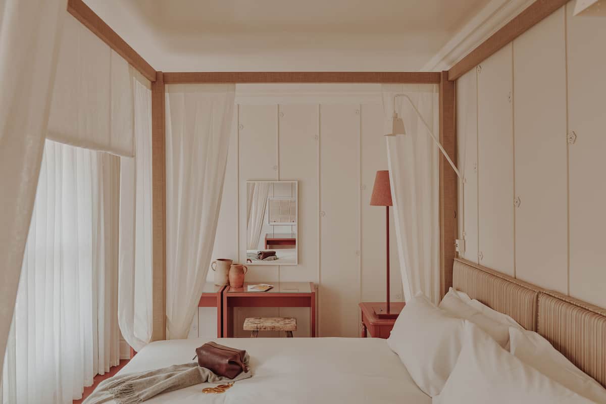 A bedroom with a bed, a desk, a lamp, and a mirror.