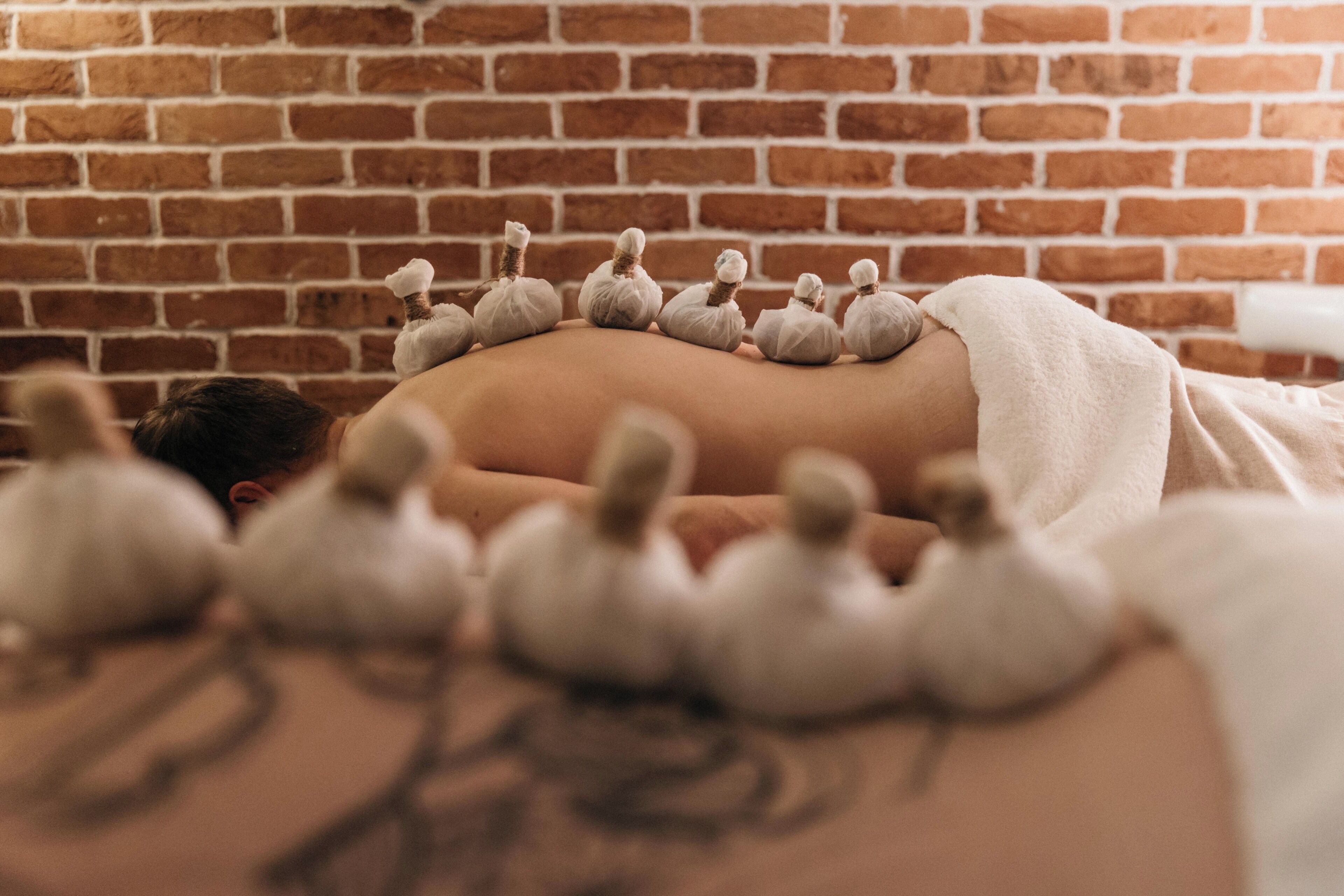 A person receiving a back massage with a row of massage stones against a brick wall.
