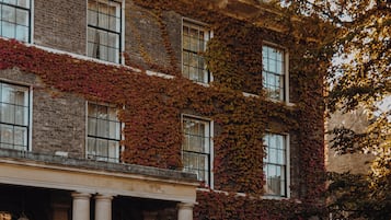 Stately building with a classical facade, featuring a covered porch and columns, surrounded by mature ivy and a well-maintained lawn.