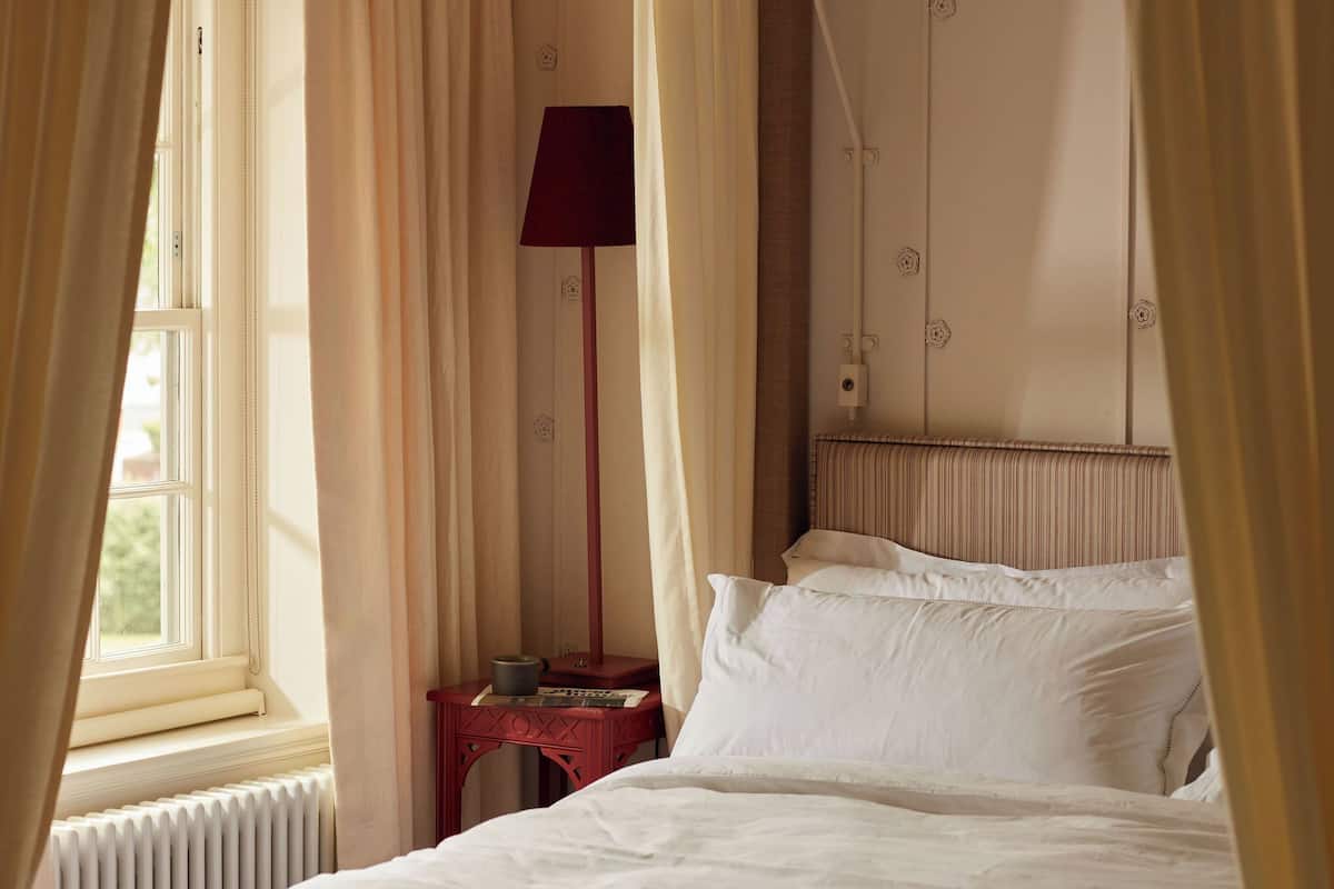 A bedroom with a bed, a nightstand, a lamp, and a window with curtains.
