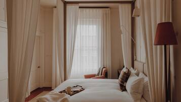 A hotel room with a large bed, a bedside table with a lamp, and sheer curtains.