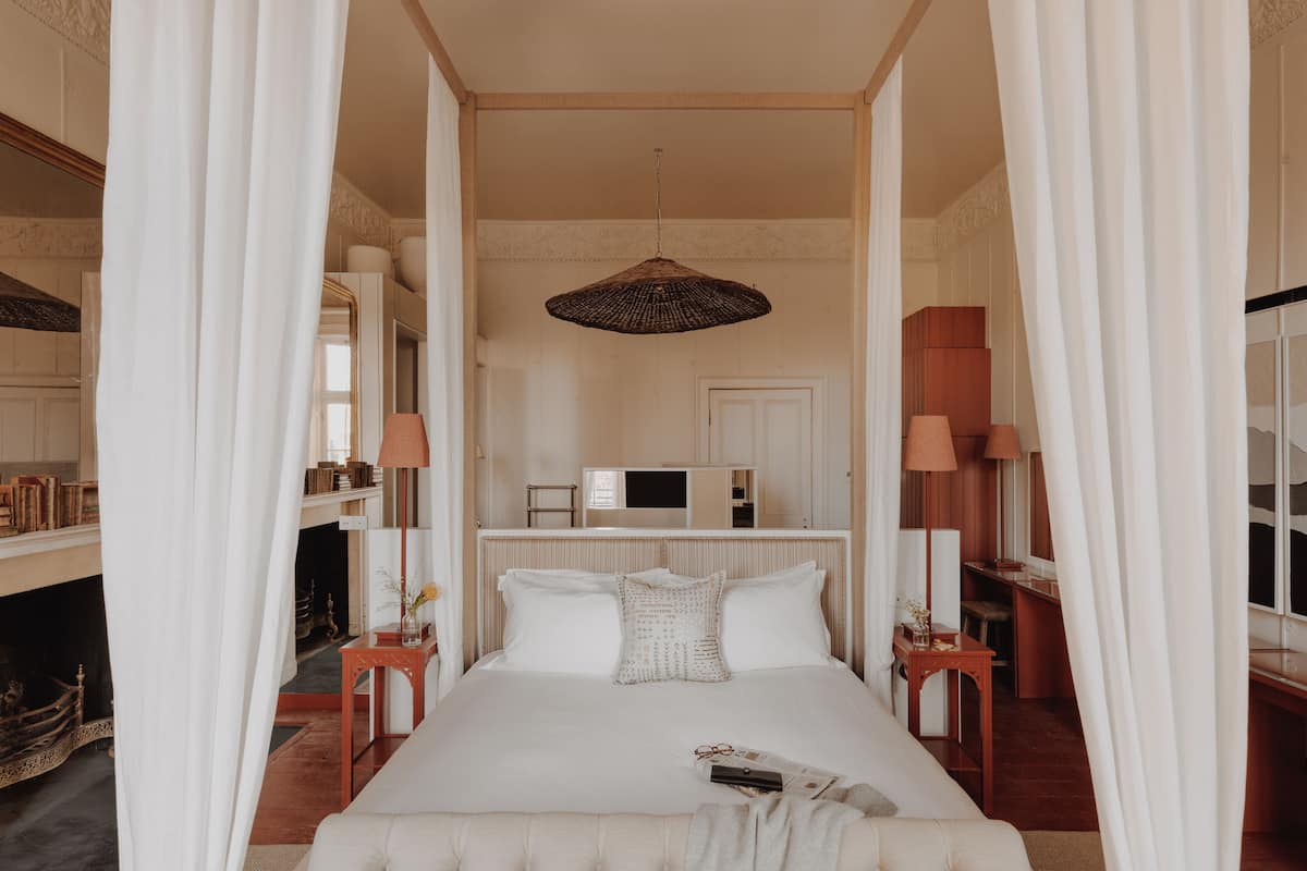 A bedroom with a canopy bed, bedside tables, a lamp, and a television in the background.