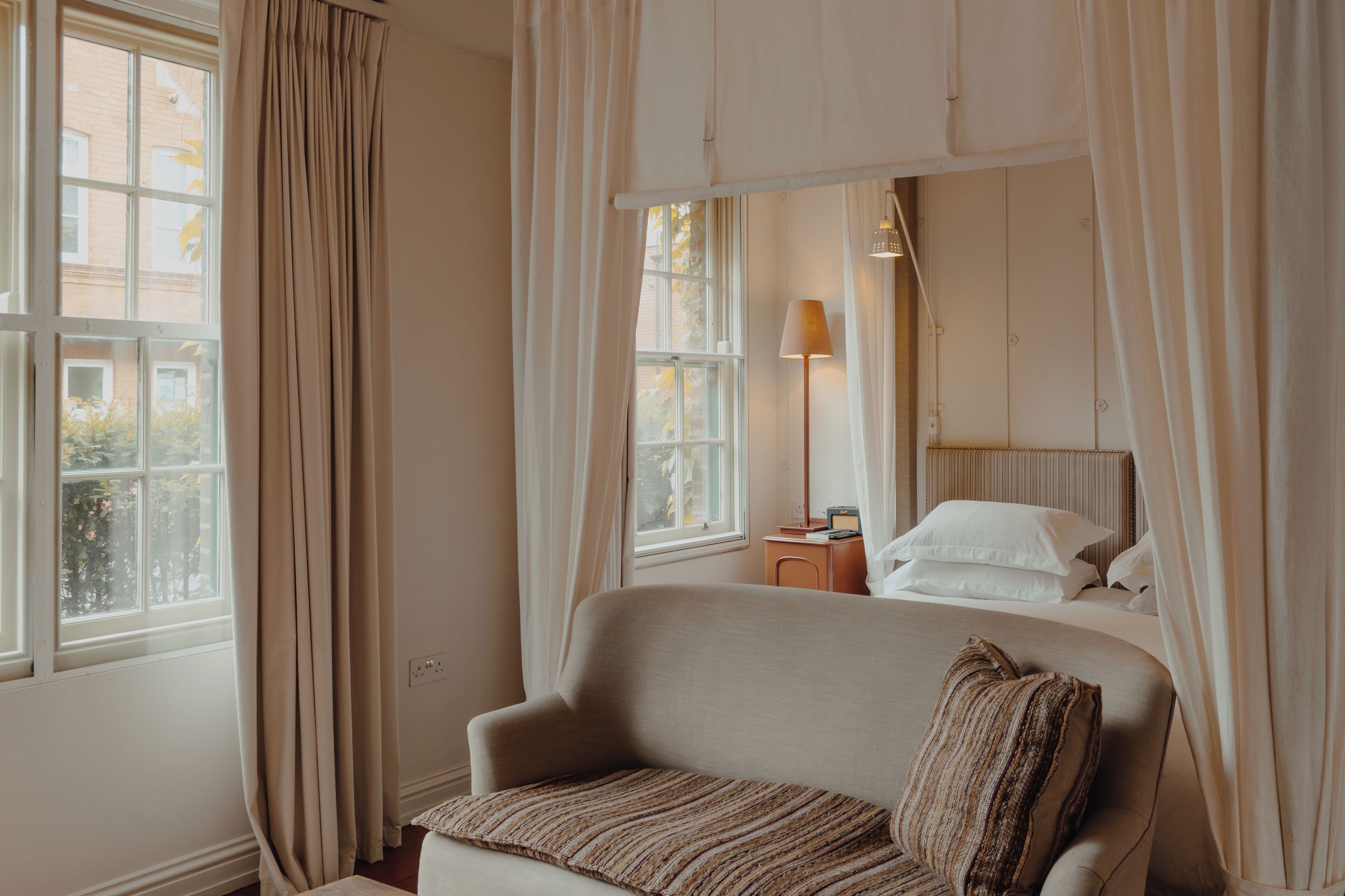A bedroom with a bed, a bedside table, a lamp, and a window with curtains.