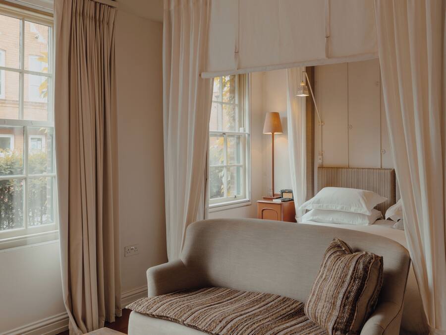 A bedroom with a bed, a bedside table, a lamp, and a window with curtains.