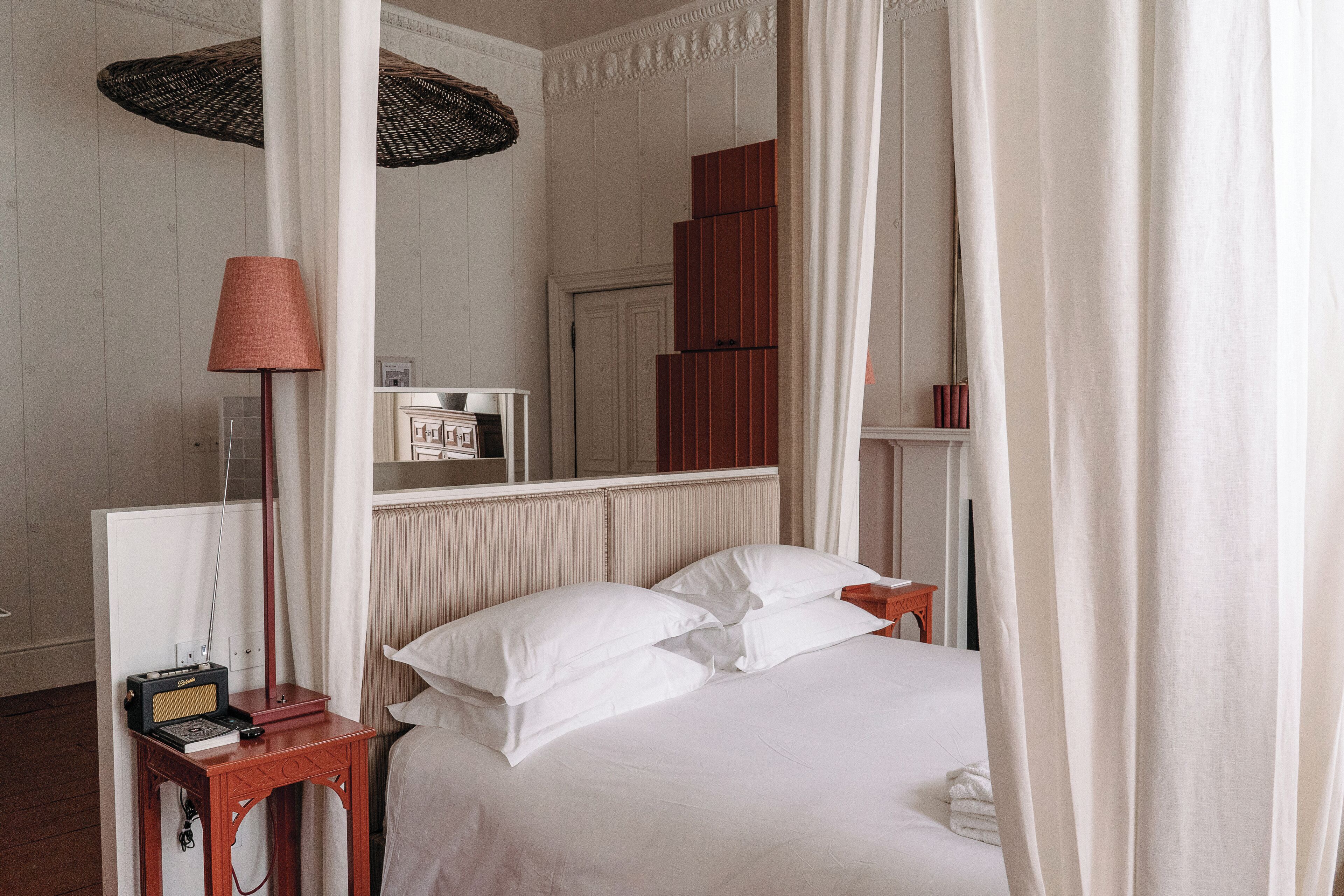 A neatly made bed with white linens, a bedside table with a lamp, and a mirror reflecting the room's decor.