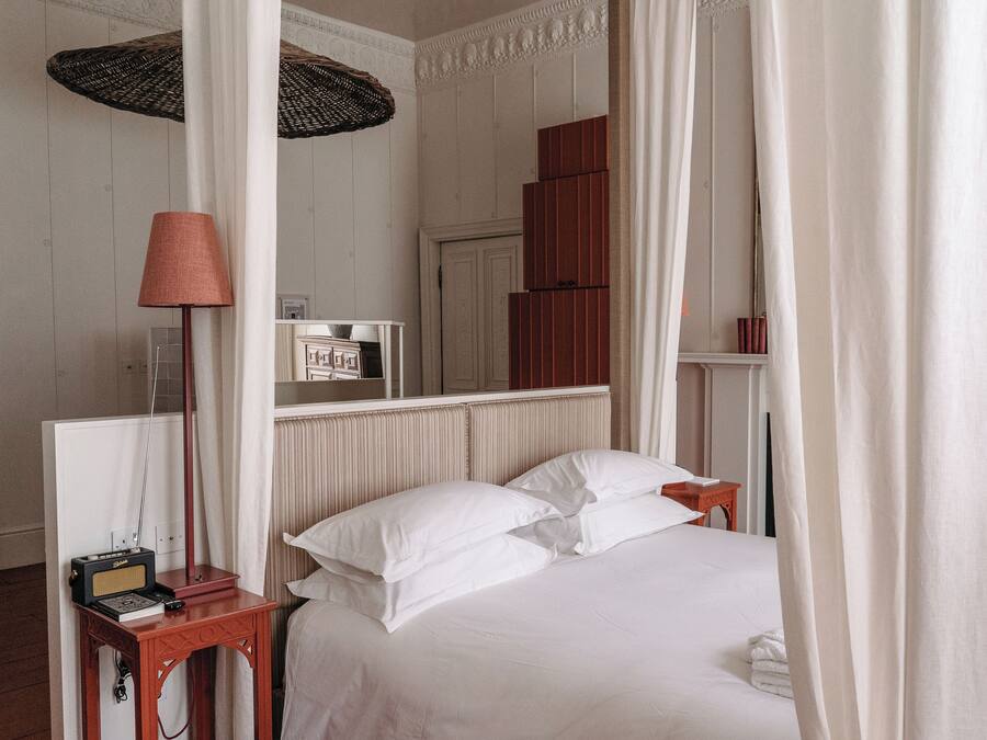 A neatly made bed with white linens, a bedside table with a lamp, and a mirror reflecting the room's decor.