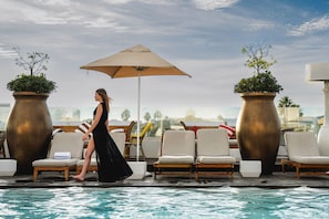A poolside area with lounge chairs, a large umbrella, and potted plants.
