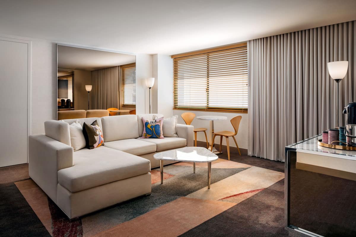 A modern living room with a beige sectional sofa, a small round coffee table, and a dining area with a table and chairs.