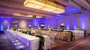 A banquet hall with long tables, clear chairs, and floral centerpieces.