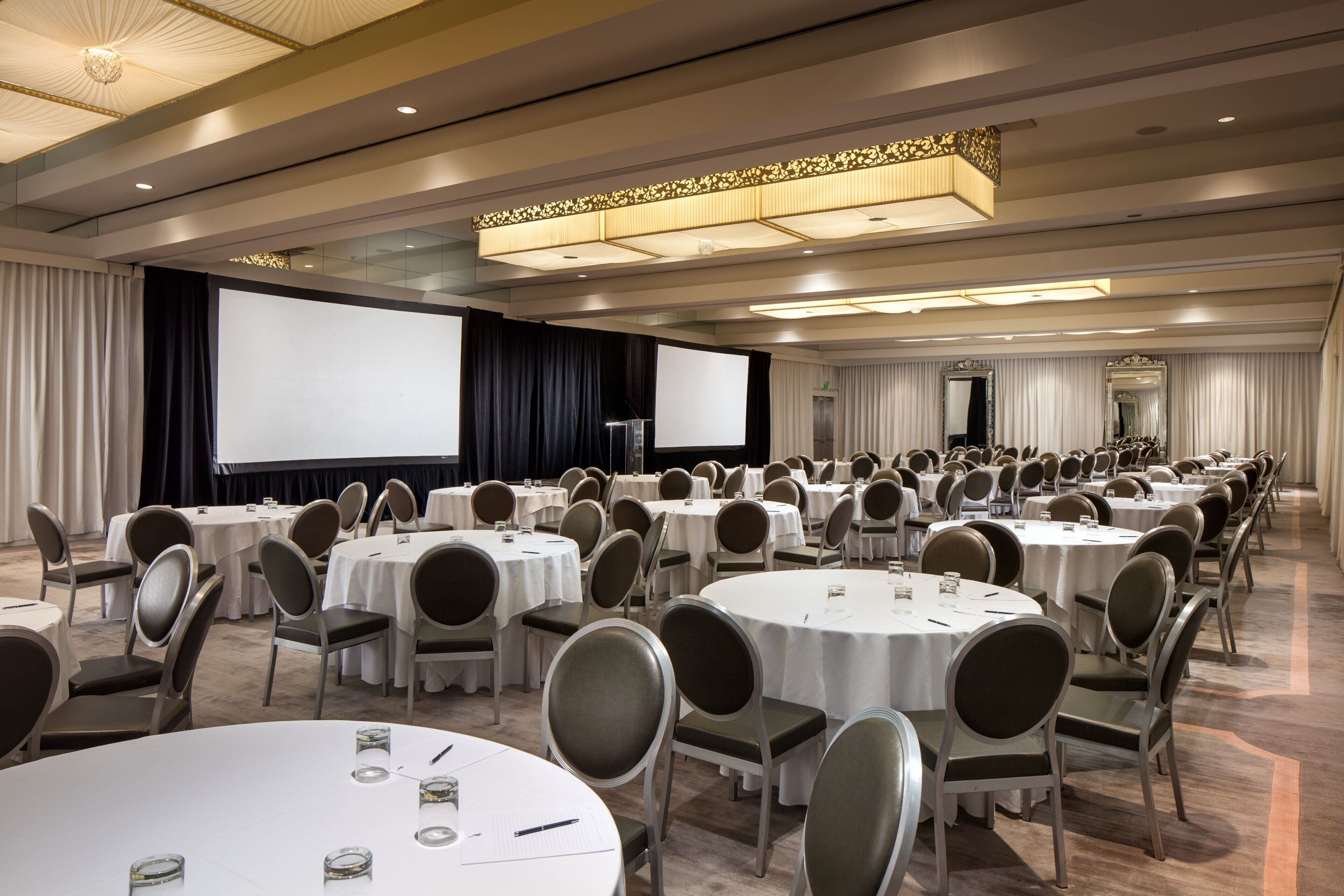Une salle de conférence équipée de tables rondes, de chaises, d’un grand écran et d’une scène.