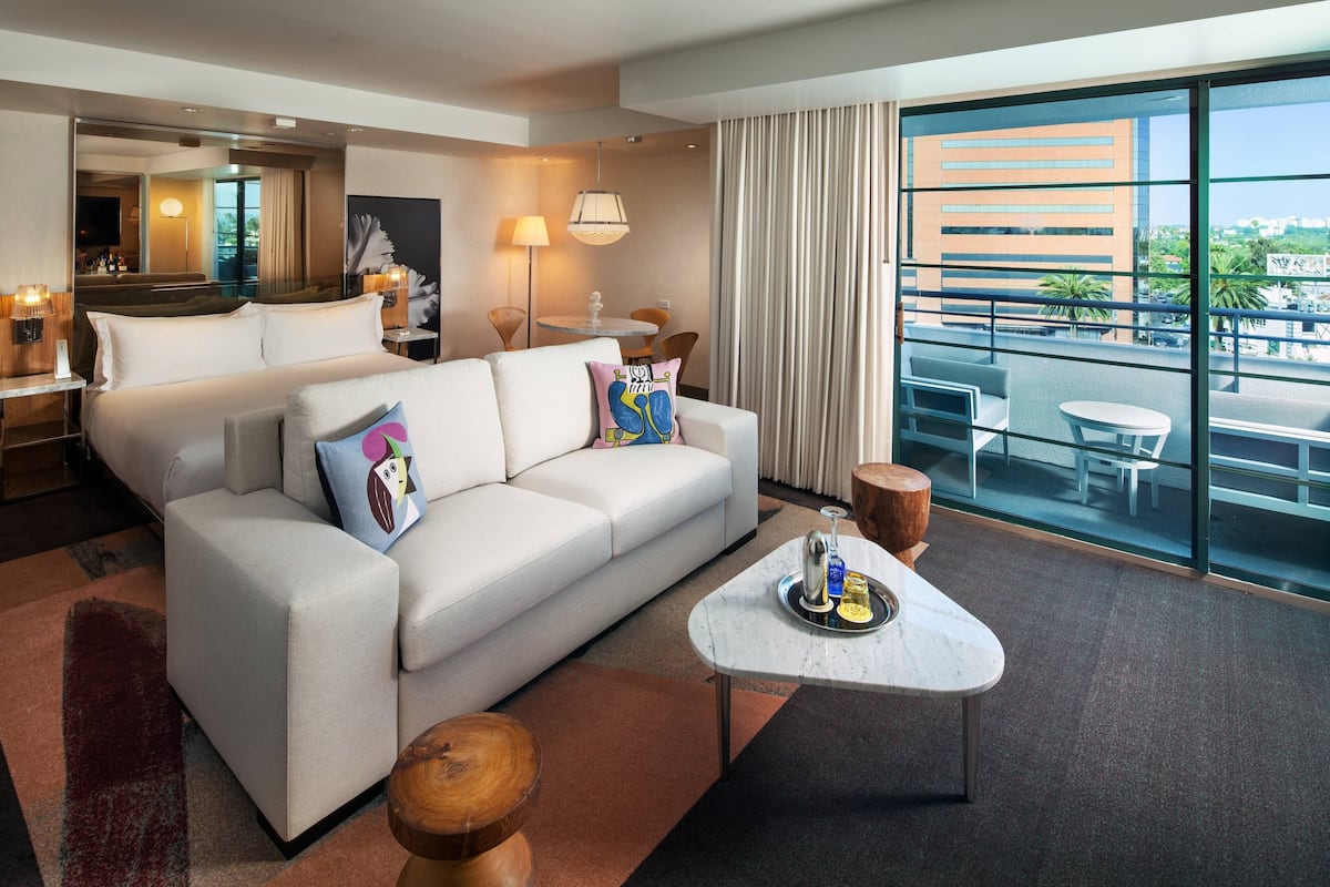 A modern hotel room with a large bed, a sofa, a coffee table, and a balcony with a view of the city.