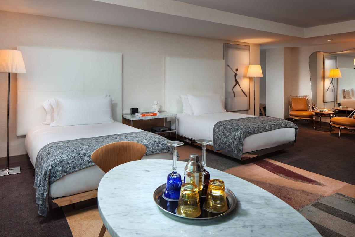 A hotel room with two beds, a sitting area with a table, and a mirror.
