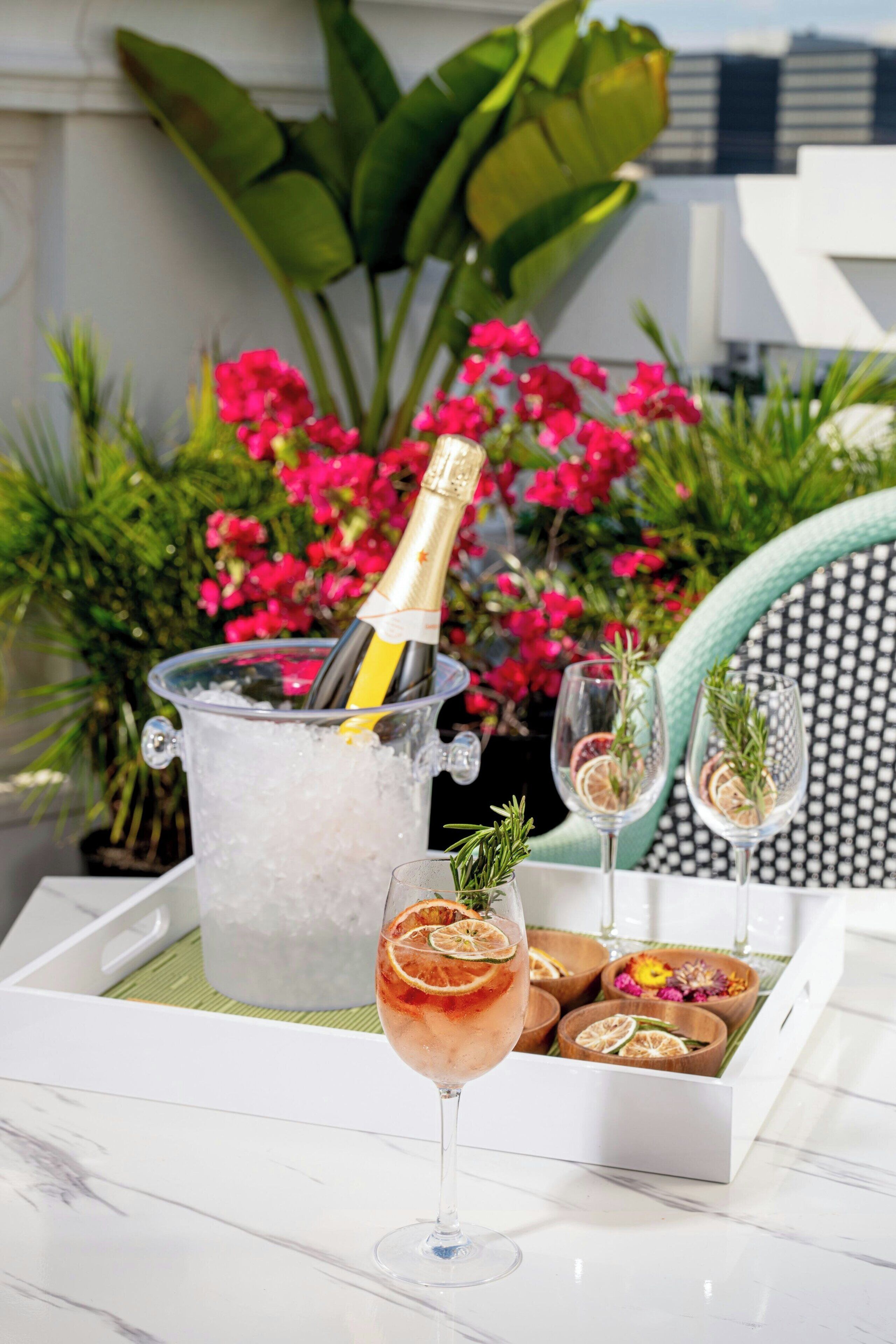 A glass of cocktail with a bottle of champagne in an ice bucket, surrounded by decorative items and a chair.