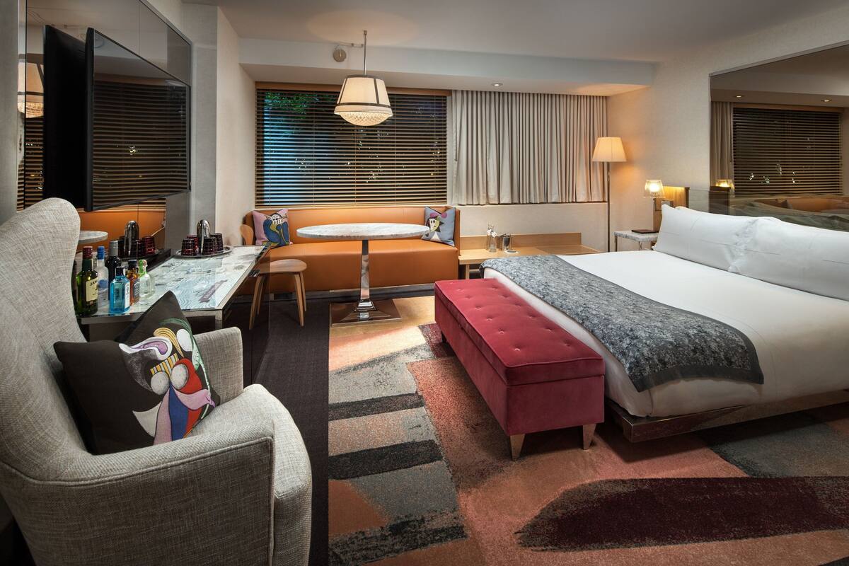 Quarto de hotel com uma cama grande, um sofá, uma mesa pequena e uma televisão.