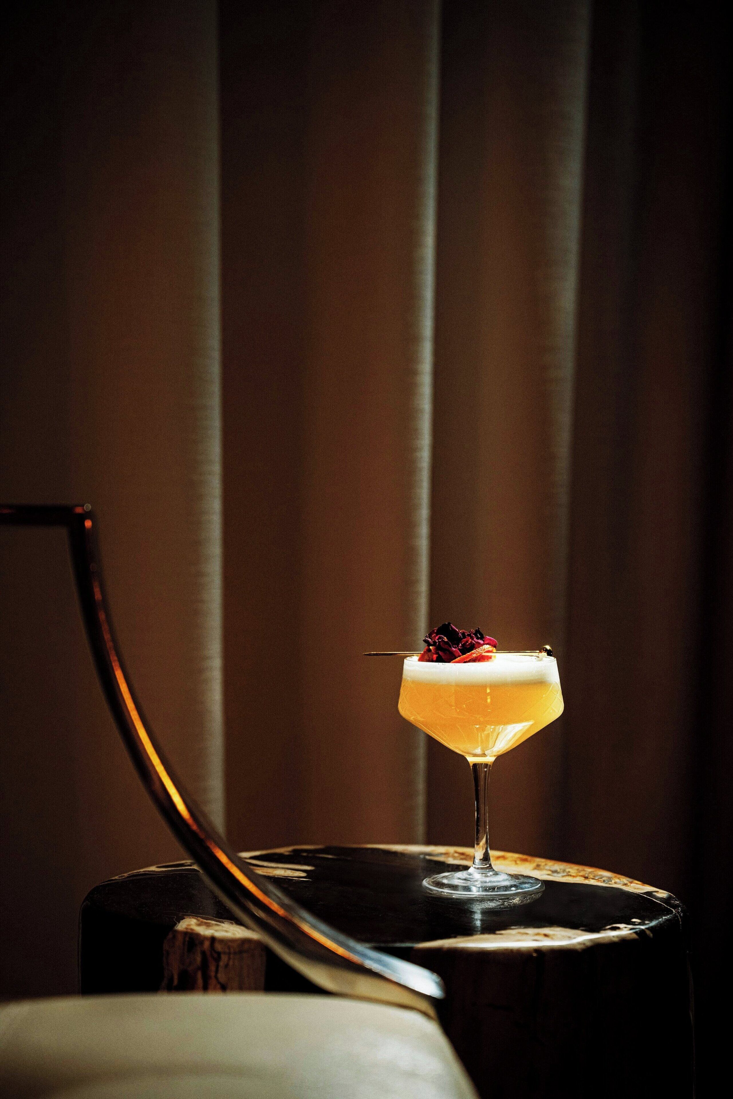 A cocktail in a glass on a wooden table with a chair leg visible.