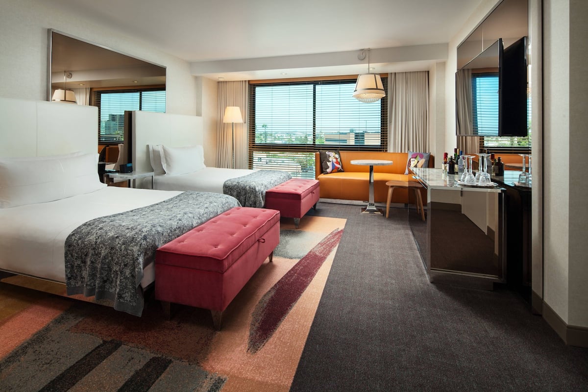 A hotel room with a large bed, a smaller bed, a desk, a chair, and a sofa.