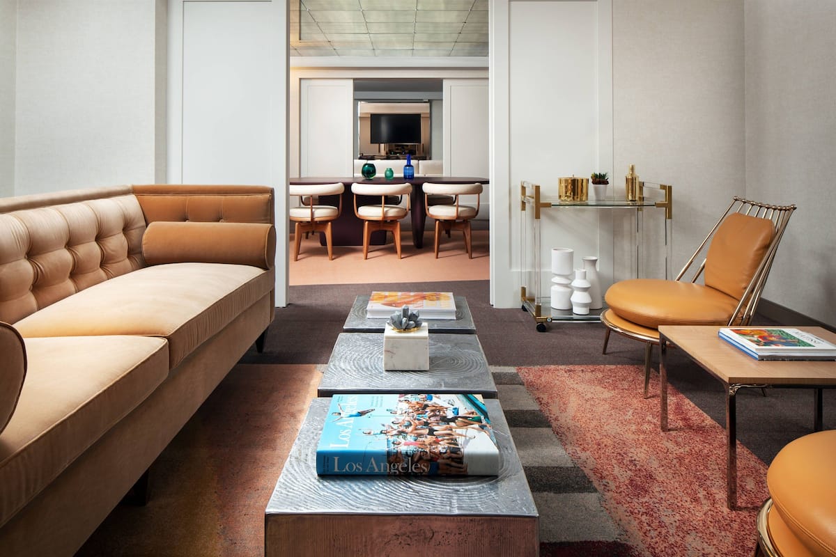 A modern living room with a sofa, coffee table, and chairs. There is a dining area with a table and chairs in the background.