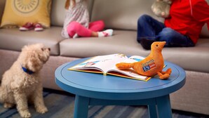 A living room with a sofa, a small round table with a book and a plush toy, and a dog. - Sonesta ES Suites South Brunswick - Princeton (Monmouth Junction)