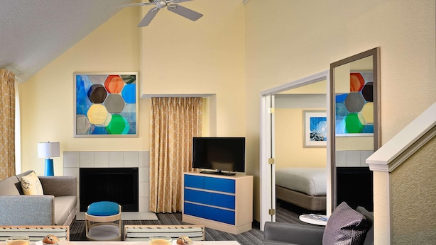 A hotel room with a sofa, a dining table with breakfast, a TV, a fireplace, and artwork on the walls. - Sonesta ES Suites South Brunswick - Princeton (Monmouth Junction)