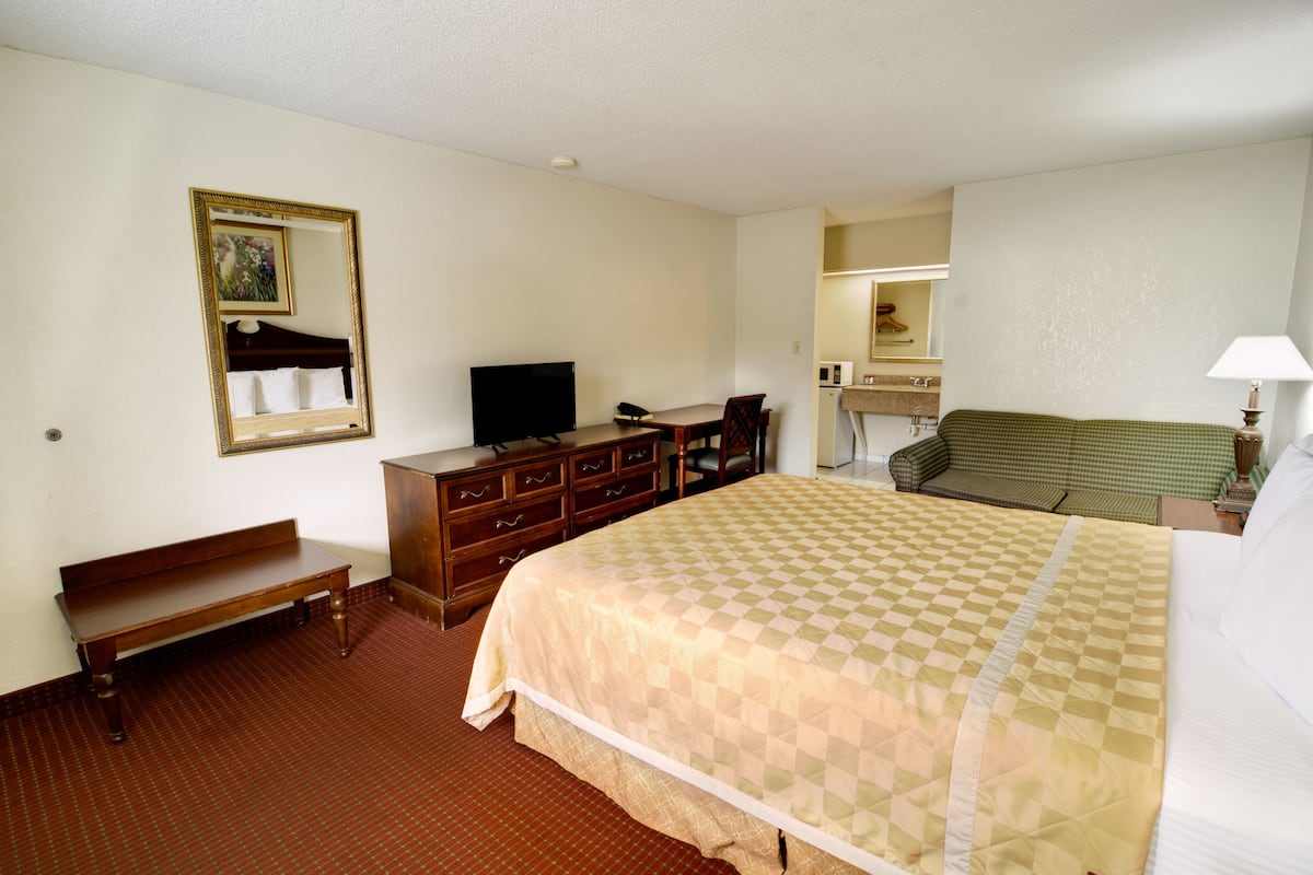 A hotel room with a large bed, a wooden bench, a dresser, a television, a green sofa, and a mirror.