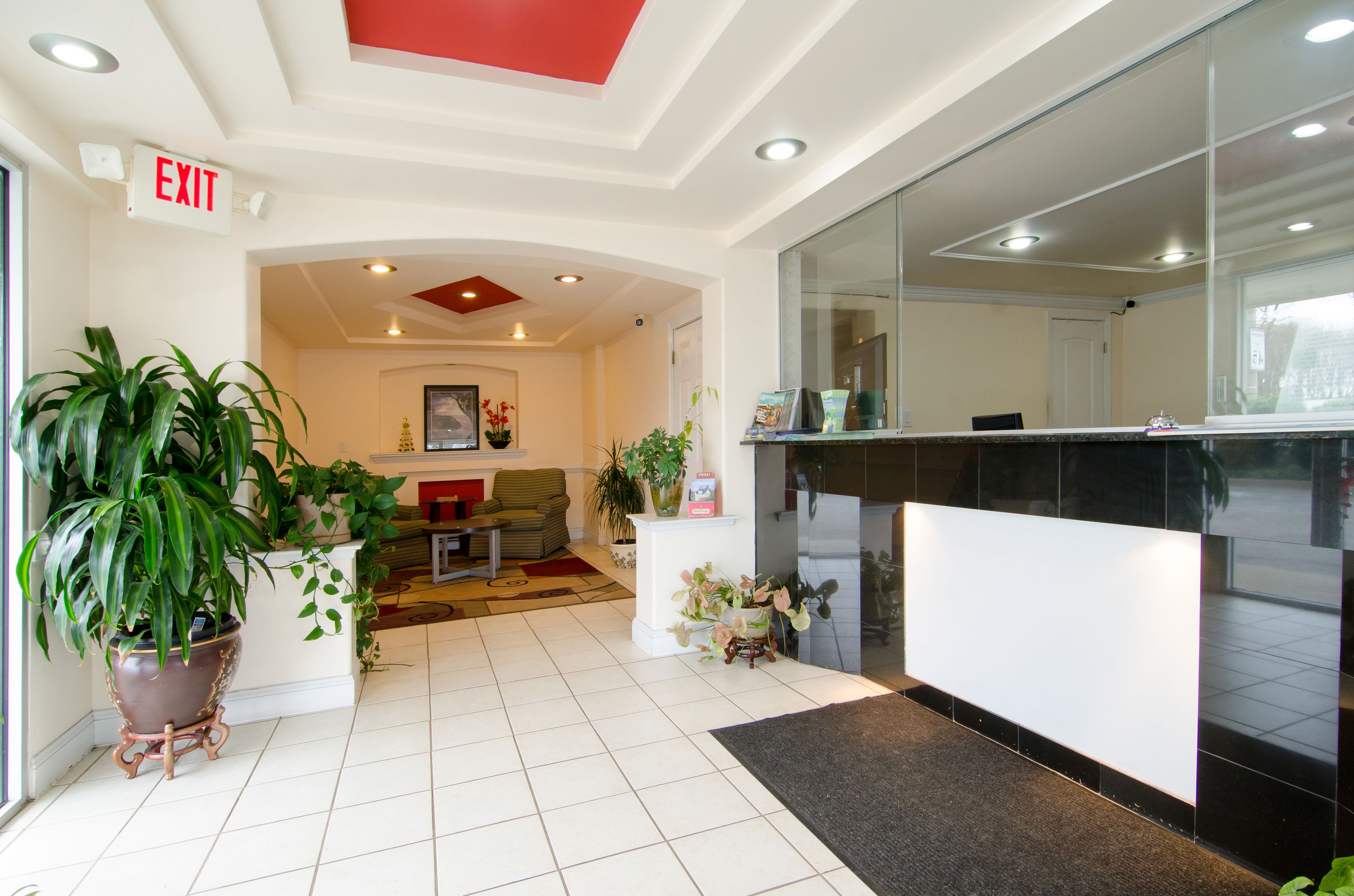 En hotellobby med en receptionsdisk, en stor krukväxt, en soffa och en utrymningsskylt.