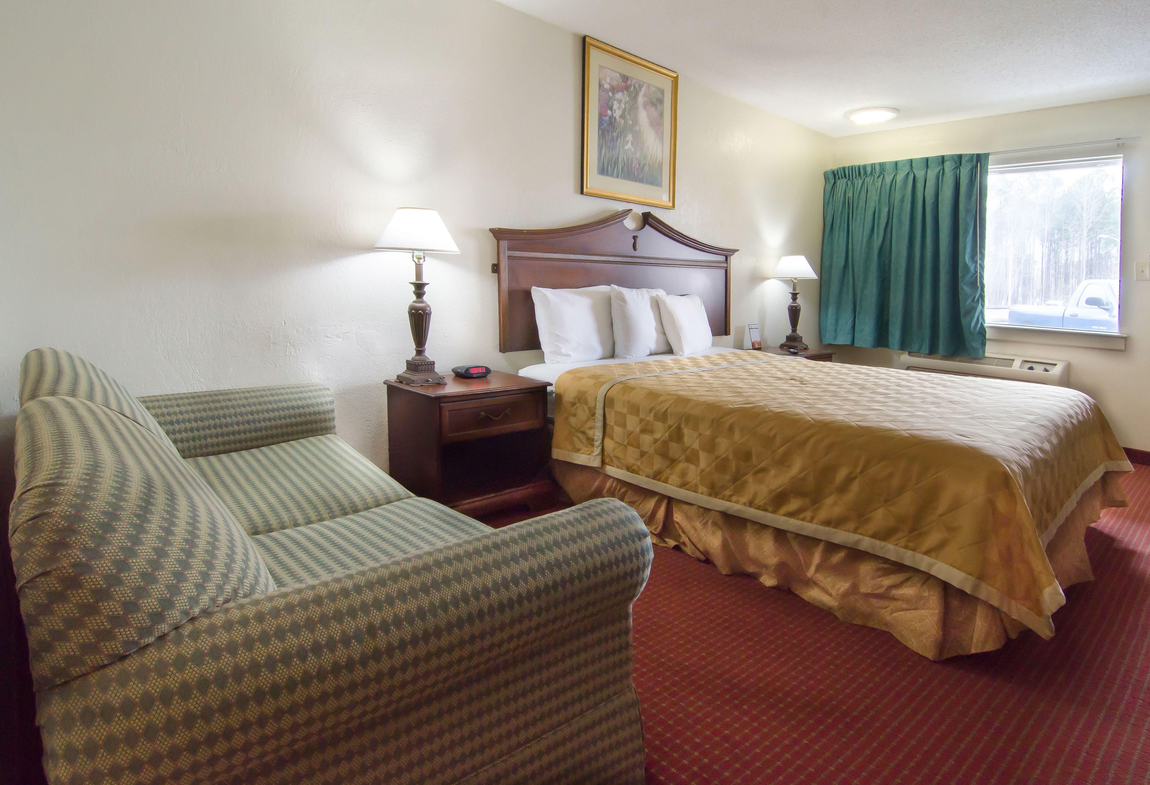 A hotel room with a bed, a chair, a nightstand, and a window with curtains.