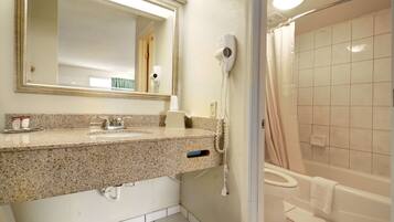 A bathroom with a granite countertop sink, a mirror, a hair dryer, and a bathtub.