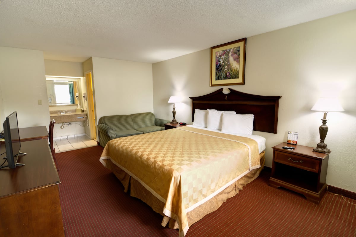 A hotel room with a large bed, a desk, a chair, a nightstand, and a bathroom visible through an open door.