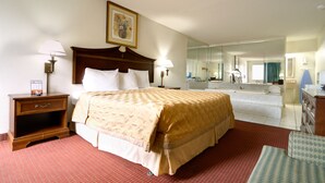 Habitación de hotel con una cama grande, una mesita de noche, un aparador, un espejo y un baño visible a través de una puerta abierta.