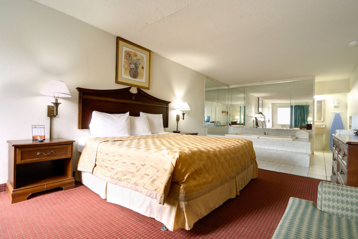 A hotel room with a large bed, a nightstand, a dresser, a mirror, and a bathroom visible through an open door.