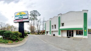 Un hotel con un cartel que indica que es un KeyWest Inn, con un diseño moderno y detalles en verde, y un estacionamiento al frente.