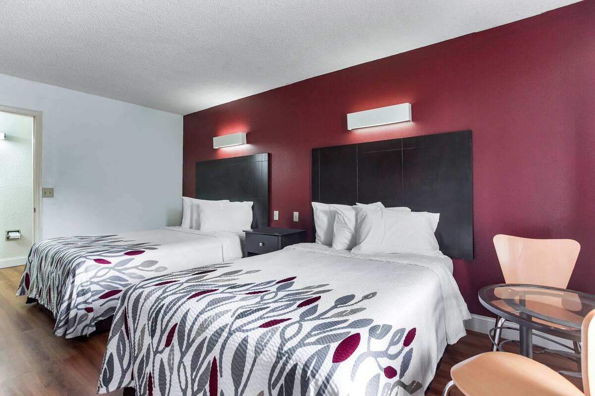 A hotel room with two beds, a round glass table, and a chair.