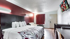 A hotel room with a large bed, a desk, a TV, and a window with curtains.