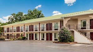 A two-story motel with a green roof, multiple rooms with dark shutters, and a parking lot.