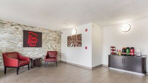 A Red Roof Inn lobby with stone wall, two red chairs, a small table, artwork, and a kitchenette with coffee makers. - Red Roof Inn Monteagle - I-24 (Monteagle)