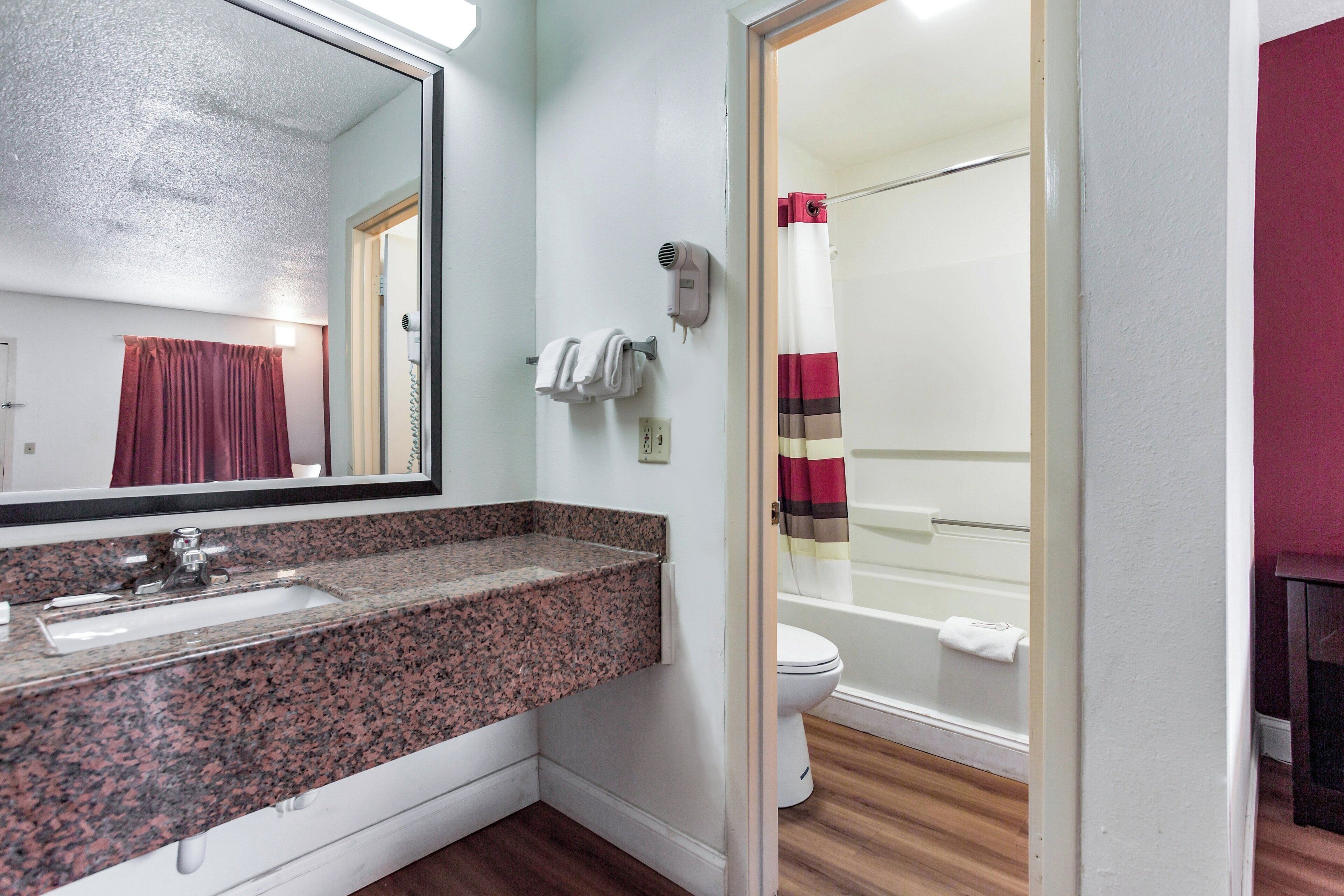 Un baño con lavamanos de encimera de granito, un espejo, toallero, secador de pelo y cortina de ducha.
