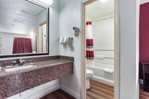 A bathroom with a granite countertop sink, a mirror, a towel rack, a hairdryer, and a shower curtain. - Red Roof Inn Monteagle - I-24 (Monteagle)