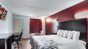 A hotel room with a large bed, a desk with a chair, a small table, and a TV on the wall.