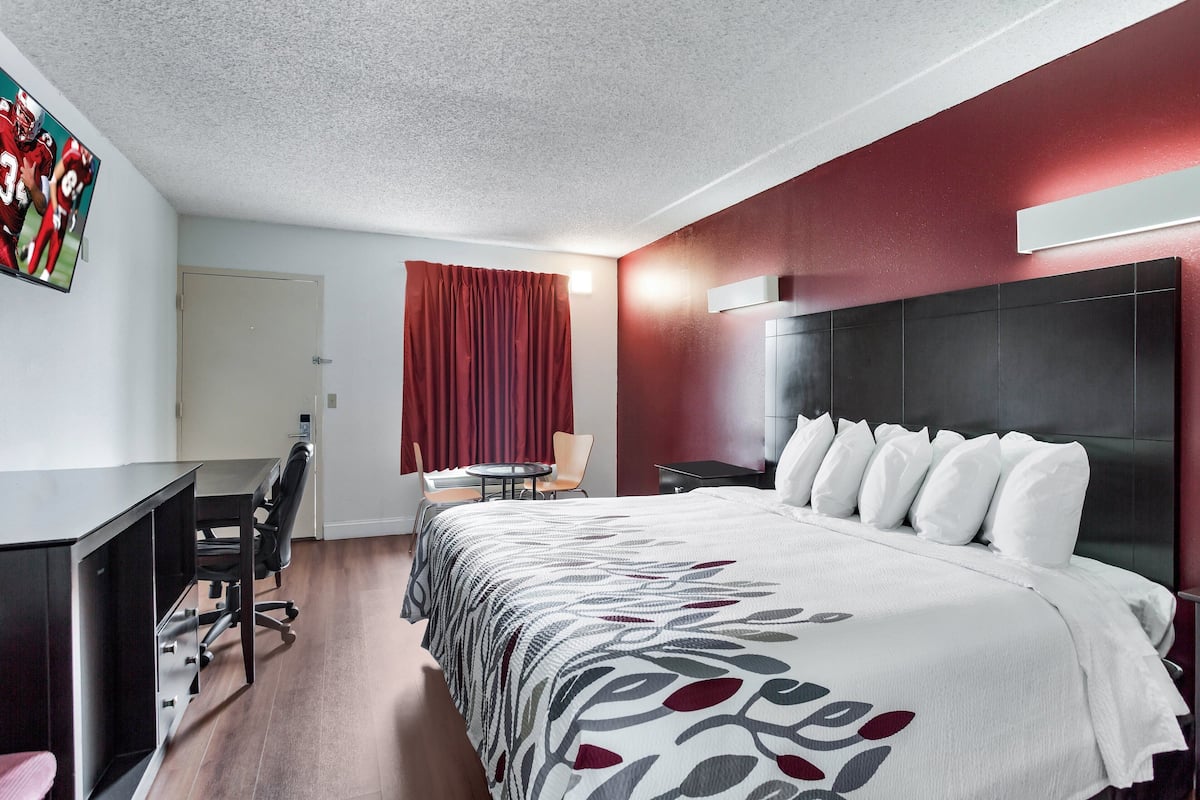 A hotel room with a large bed, a desk with a chair, a small table, and a TV on the wall.