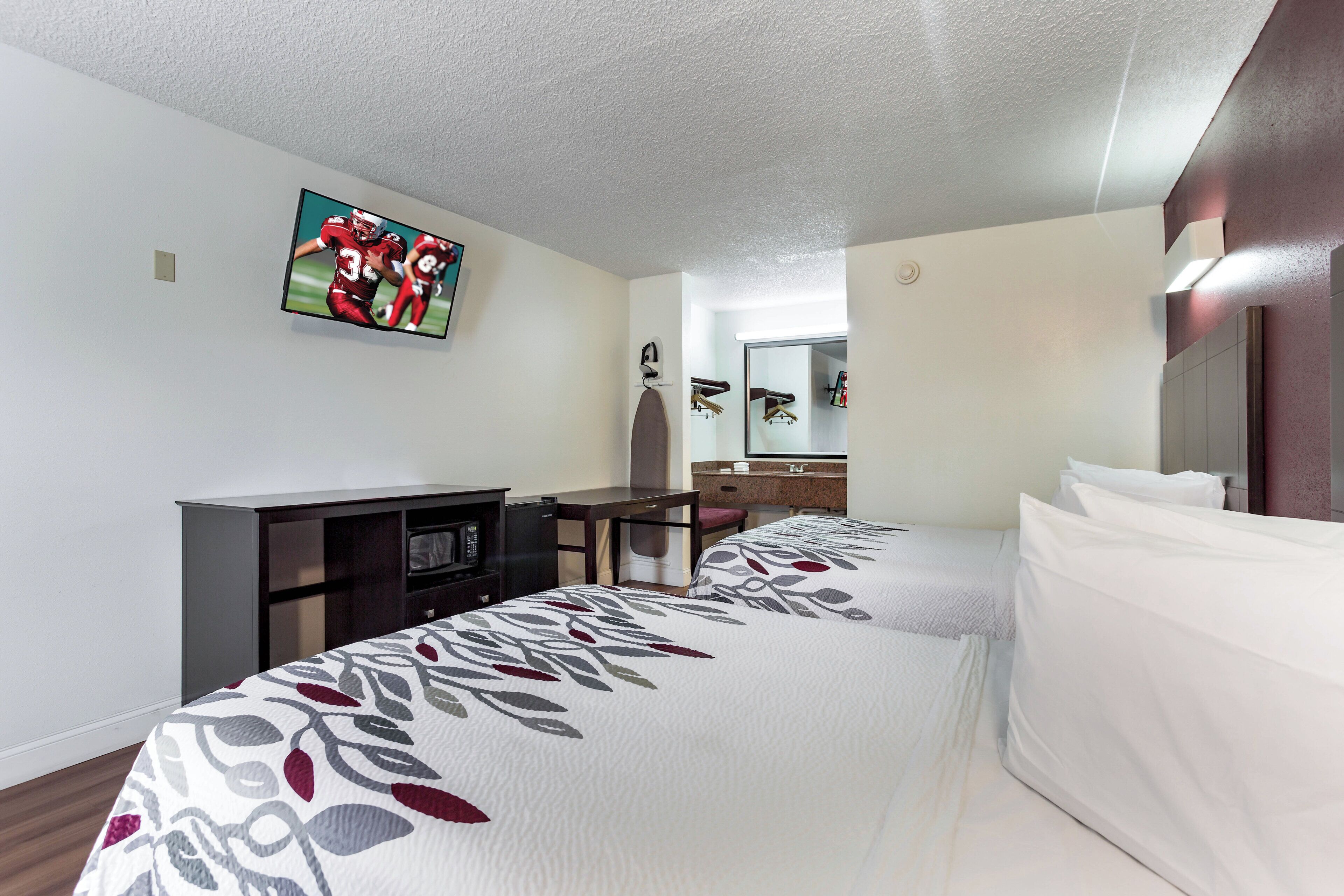 Une chambre d’hôtel avec un lit, un bureau, une télévision et un miroir.
