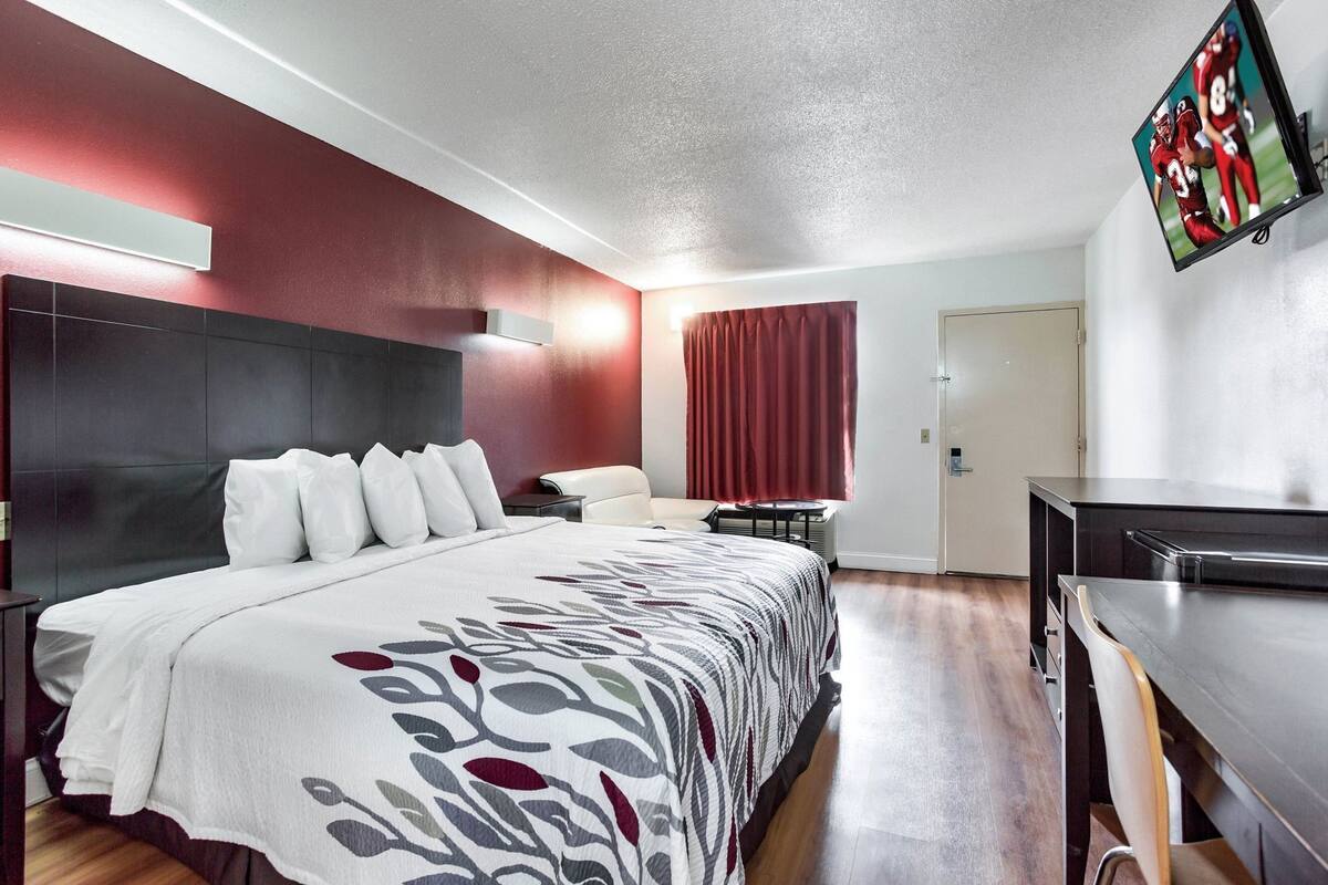 A hotel room with a large bed, a desk, a TV, and a door.