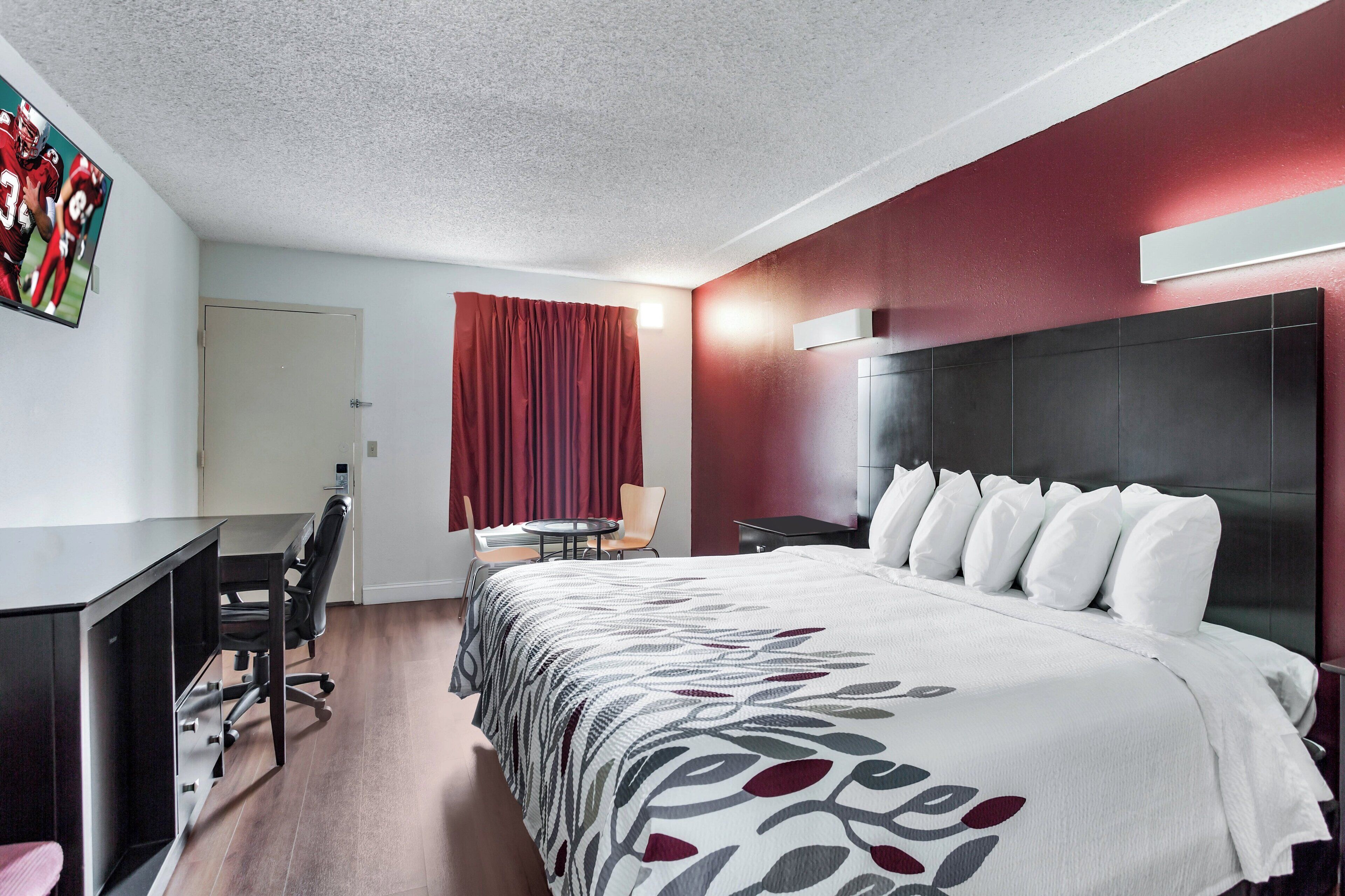 A hotel room with a bed, a desk, a chair, a small table, and a window with curtains.