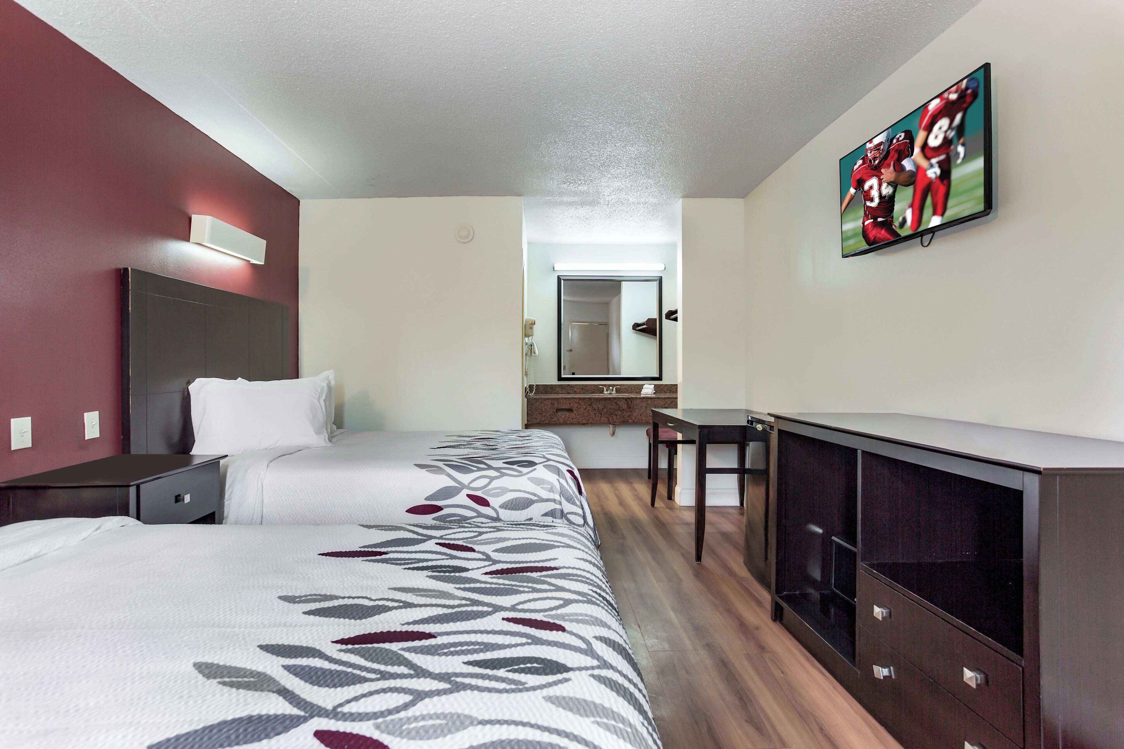 Ein Hotelzimmer mit zwei Betten, einem Schreibtisch, einem Sessel, einem Fernseher und einem durchgegangenen Tür sichtbaren Badezimmer.