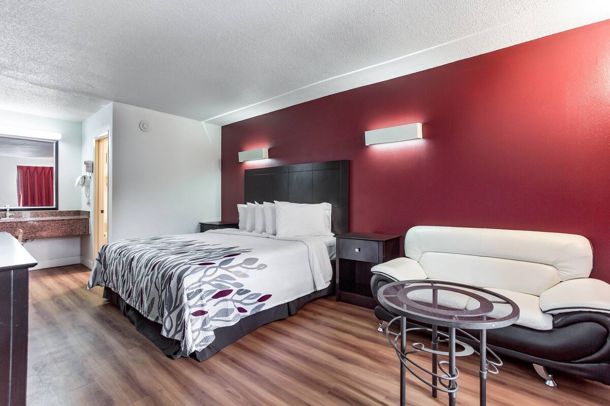 A hotel room with a bed, a chair, a small table, and a nightstand.