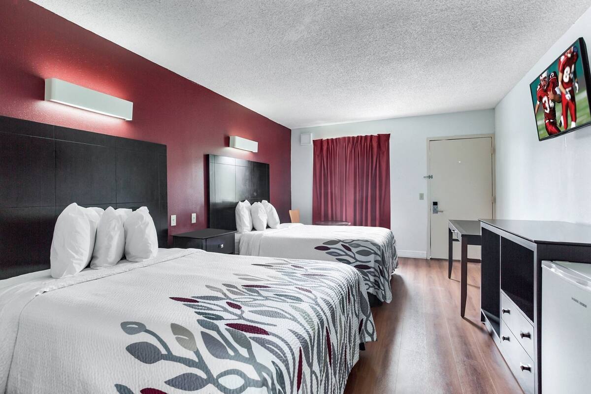 A hotel room with two beds, a desk, a TV, and a red curtain.