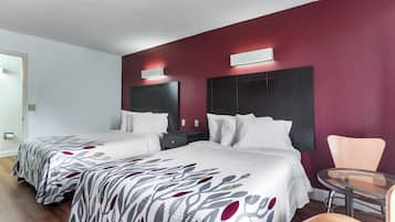 A hotel room with two beds, a small table, a chair, and a red accent wall.
