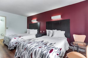 Una camera d'albergo con due letti, un tavolino, una sedia e una parete decorata di rosso.