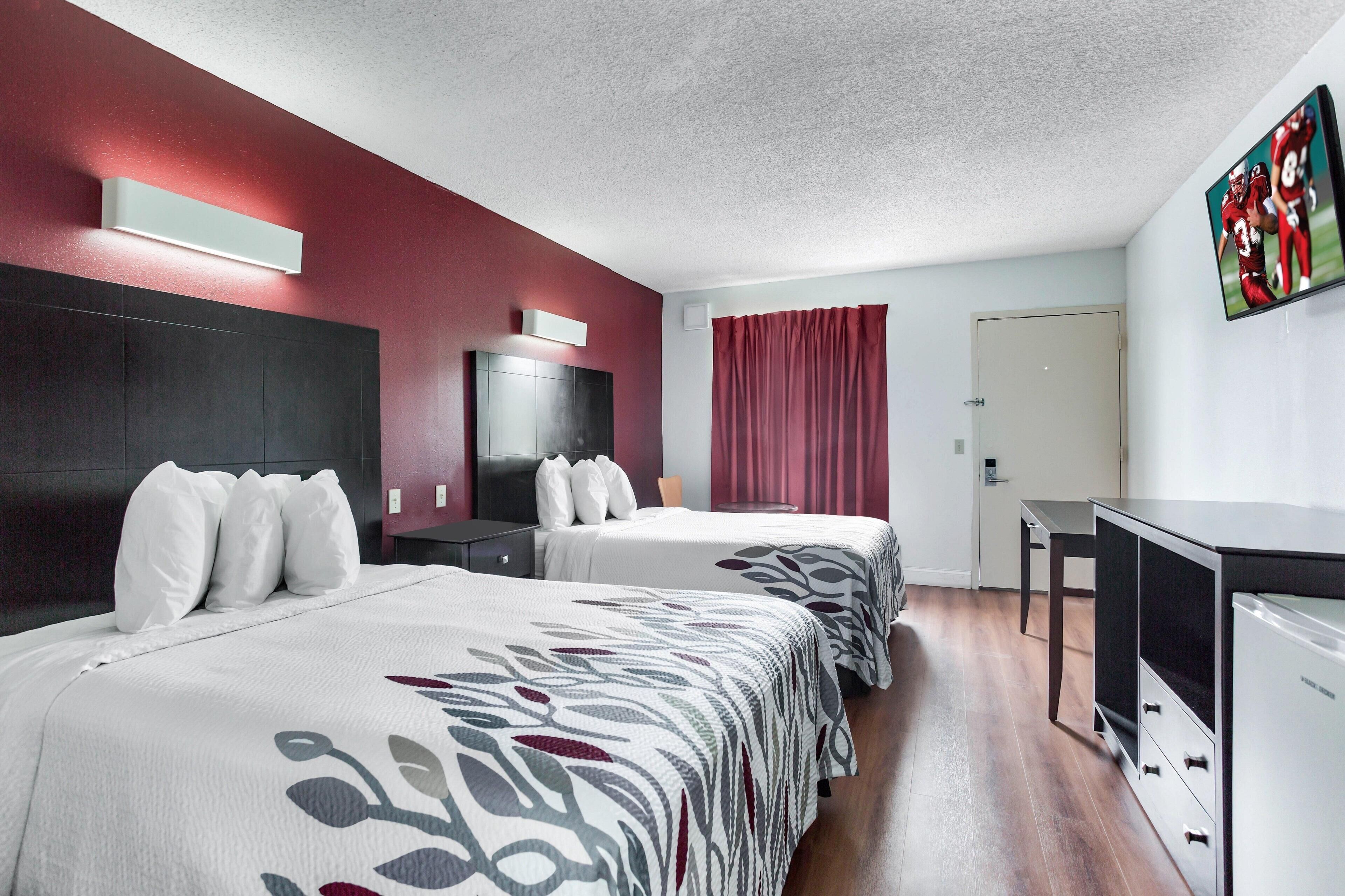 A hotel room with two beds, a desk, a TV, and a door.