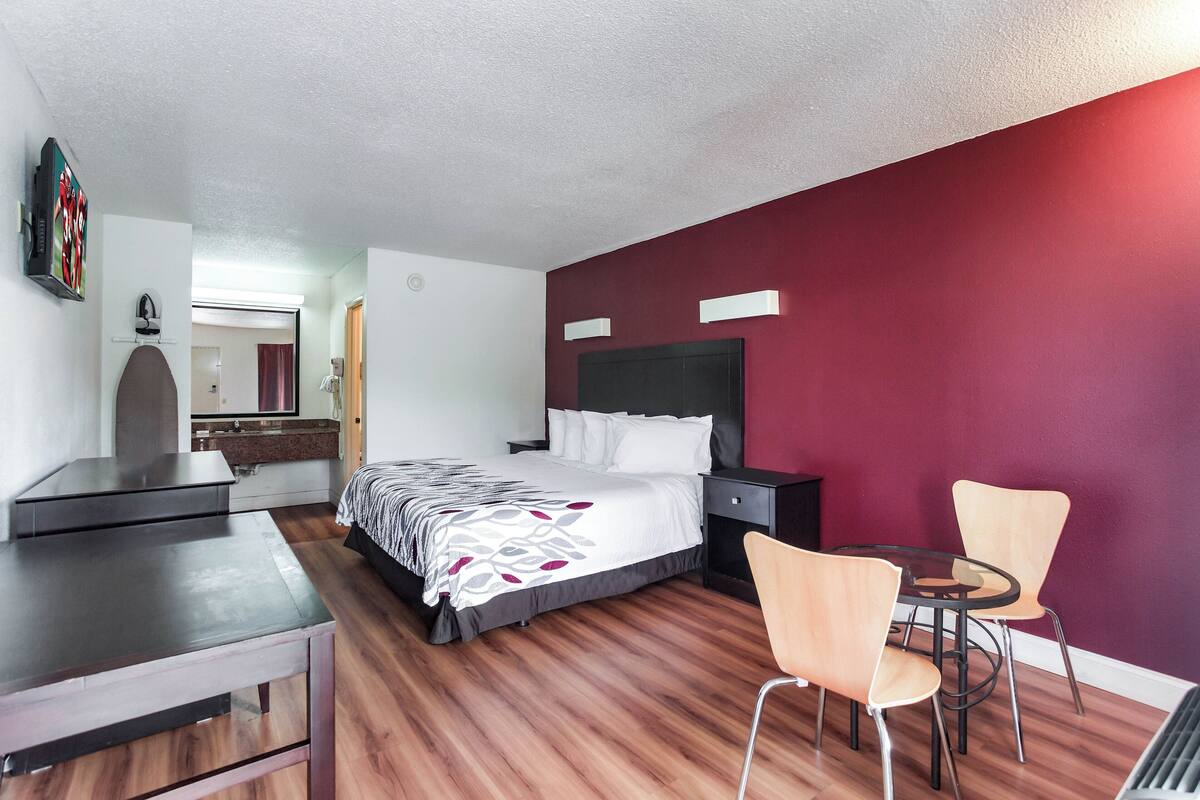 A hotel room with a bed, bedside table, chair, and a small dining table with chairs.