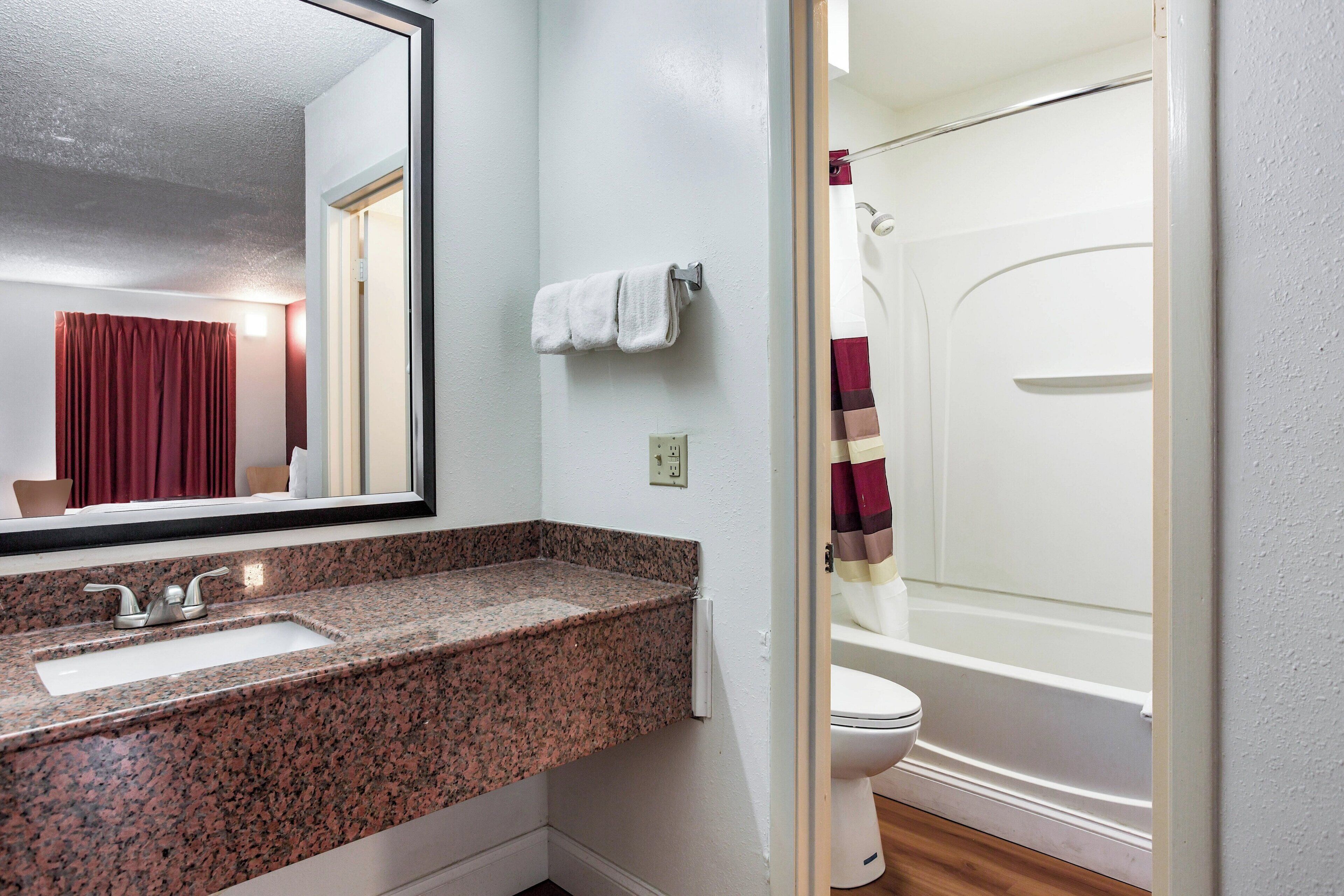 A bathroom with a granite countertop sink, a mirror, a towel rack, and a shower curtain.